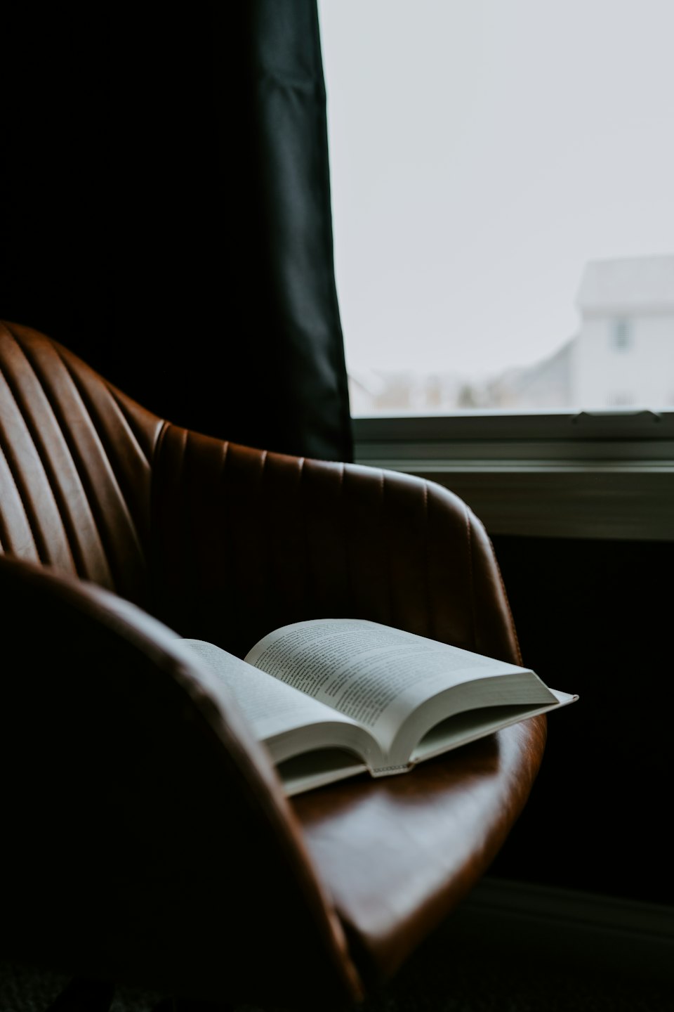 Home Un libro aperto posato su una poltrona di pelle vicino a una finestra.